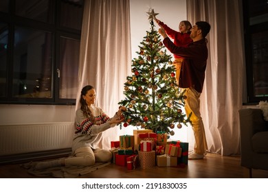 family, winter holidays and people concept - happy mother, father and little daughter decorating christmas tree at home - Powered by Shutterstock