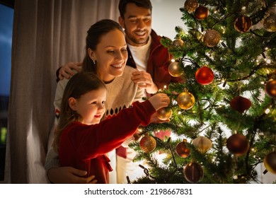 family, winter holidays and people concept - happy mother, father and little daughter decorating christmas tree at home - Powered by Shutterstock