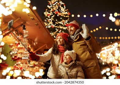 family, winter holidays and technology concept - happy mother, father and little daughter taking picture by smartphone on selfie stick at christmas market on town hall square in tallinn, estonia - Powered by Shutterstock