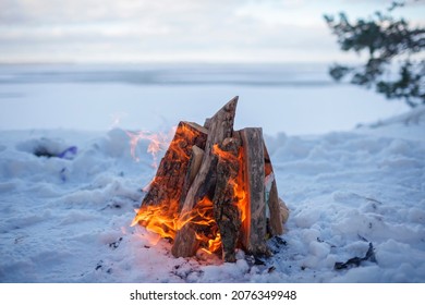 Family winter picnic. Bonfire on the shore of a frozen lake during a winter family walk in the forest, outdoor family weekend at snowing day, winter travel