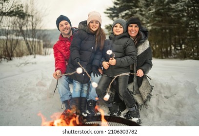 A Family Winter Picnic. Happy Friends Sit Around Campfire In Forest And Fry Marshmallows During A Winter Trip At Weekend With The Family Child