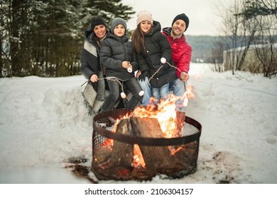 A Family Winter Picnic. Happy Friends Sit Around Campfire In Forest And Fry Marshmallows During A Winter Trip At Weekend With The Family Child