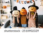 Family in witch hats and carved pumpkins, having fun at home for halloween. Smiling, crafting, and decorating together, creating special memories