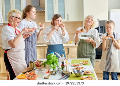 Family, Women Of Different Generations Enjoy Eating Pizza Together In Kitchen, After Cooking Time. Mature Grandwomen And Children Standing Next To Table With Food, Wearing Apron