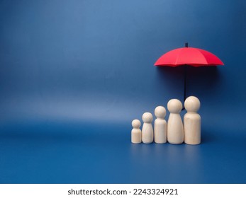 A family of wooden dolls are hiding under a red umbrella, protecting wooden peg dolls, planning, saving families, preventing risks and crises, health care and insurance concepts. - Shutterstock ID 2243324921
