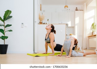 Family Yoga Class - A Young Mother And Son Of A Schoolboy In A Cobra Pose On The Floor Against The Background Of White Kitchen