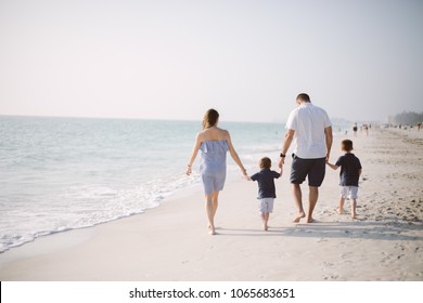 Family with Young Boys Holding Hands and Walking Down the Coastline at the Beach