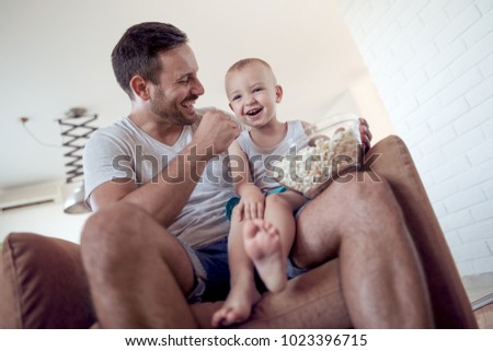Family,childhood,fatherhood,technology and people concept-happy father and little son with popcorn feed each other and having fun at home.