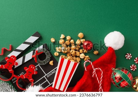 Family-oriented New Year's debut with children's theme. Top view of clapper, gingerbread man-inspired glasses, popcorn in paper box, Santa's hat, balls, wreath, sweets on green backdrop with ad space