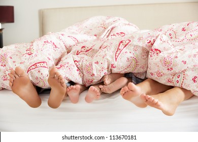 Family's Feet Poking Out From Duvet In Bed