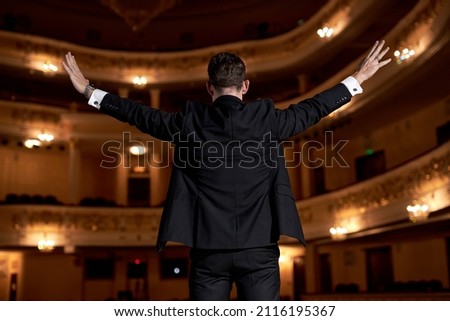 Famous American Entertainer Stands on Stage, Greets Audience, Starts Performance. Presentation Speaker Giving Talk. Handsome European Caucasian Guy In Formal Suit Is Successful Talented Couch