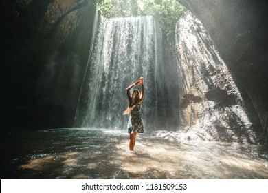 Famous Bali waterfall in the cave Tukad Cepung. Young girl tourist discover the beauty of earth