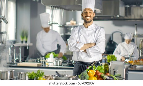 Famous Chef of a Big Restaurant Crosses Arms and Smiles in a Modern Kitchen. His Staff in Working in the Background. - Powered by Shutterstock