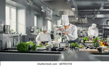Der berühmte Küchenchef arbeitet mit seiner Hilfe in einer großen Küche. Die Küche ist voll von Essen, Gemüse und Kochgeschirr. Er probiert Geschmack.