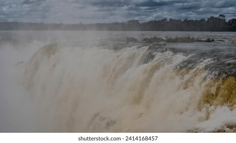 The famous Devil's Throat Waterfall. Close-up. Streams of water descend from the ledge of the river into the abyss. Spray, foam, fog. Clouds in the sky. Iguazu Falls. Argentina