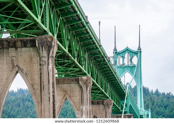 Famous gothic arched rope support of a long truss\
transportation St Johns Bridge with concrete columns and stretch\
marks that support the bridge across Willamette River in Portland\
industrial area