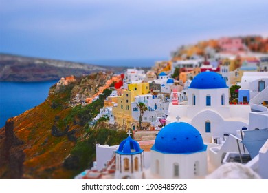 Famous greek iconic selfie spot tourist destination Oia village with traditional white houses and church in Santorini island on sunset in twilight, Greece. Toy camera tilt shift miniature effect