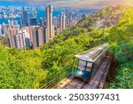 The famous green tram on the slope of Victoria Peak in metropolis Hong Kong passes, lifting up visitors to the observation deck at the top peak.