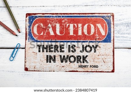 Famous Henry Ford quote THERE IS JOY IN WORK. Metal CAOTION plate with text on a white wooden background.