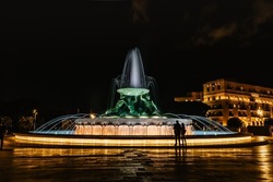 Famous Illuminated Tritons Fountain At Night,three Bronze Mythological Tritons Sculptures Holding Up Huge Basin,modern Landmark Of Valletta.Long Exposure Photo,blurred People In Motion.Night City