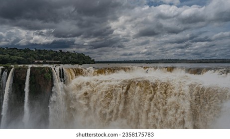 The famous impressive Devil's Throat Waterfall. Powerful streams of foaming water collapse into the abyss. Spray and fog. Clouds in the sky. Iguazu Falls. Argentina.