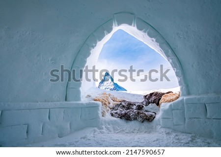 Famous matterhorn peak against sky seen through igloo. Snow covered fur at entrance of ice house. Interior of frozen hut in alpine region during winter.