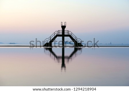Famous Saint-Malo outdoor swimming pool with jumping platform and its symmetrical reflection in hight tide ocean water, Brittany, France