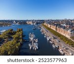 Strandvägen, famous street of Stockholm, early autumn, from above, with late 19th century buildings and an alley of green trees. Boats at dock. People walking