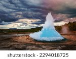 Famous Strokkur fountain geyser hot blue water eruption with cloud sky and surrounding Icelandic landscape, Iceland
