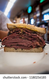 Famous Thick Cut Pastrami Sandwhich In New York City At A Deli With Great Meet Great Cuts On Rye Bread With Oils Dripping At A Diner While Hand Held And Half Cut For Easy Eating