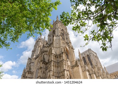 The famous towers of York Minster in the summer sunshine.  Tree foliage and a blue sky completes the scene.
