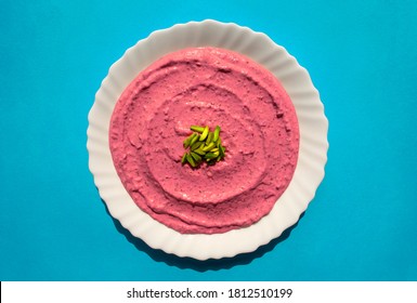 Famous traditional Arabic cuisine - Beet hummus in a white plate on blue background. Arabic beet and pomegranate labneh or yogurt. Top view