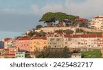 Famous viewpoint Miradouro da Senhora do Monte with city view of Lisbon timelapse during sunset with colorful houses around, Lisbon, Portugal. Clouds on the sky over green trees