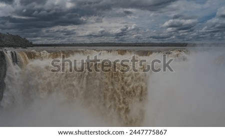The famous waterfall is the Devil's Throat. Streams of bubbling foaming water collapse into the abyss. Splashes, fog. Clouds in the blue sky. Green vegetation on the river bank. Iguazu Falls.Argentina