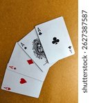 A fan of four playing cards—Ace of Clubs, Ace of Spades, Ace of Diamonds, and Ace of Hearts—spread out on a light brown surface.
