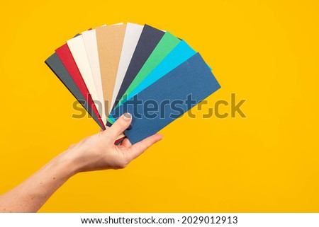 Fan of palette. Color scheme in female hands. Female hand with multi-colored cards. concept is choice of color. Fan palette in hand of designer. Multi-colored palette on yellow background.