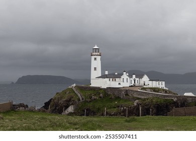 Fanad Head Lighthouse in County Donegal, Ireland, during an approaching storm. The sky and ocean blend into muted grey tones, highlighting the stark white of the lighthouse - Powered by Shutterstock