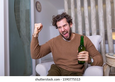 Fanatic Sports Fan Man Watching Soccer Game On Tv Celebrating. Attractive, Happy Guy Watching Football, Celebrating Victory Of His Favorite Team, Having Beer And Pop Corn, Sitting In Living Room
