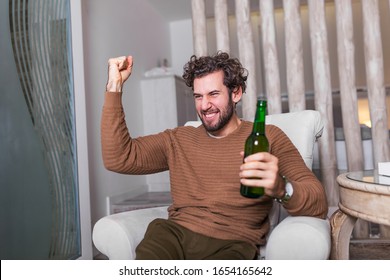 Fanatic Sports Fan Man Watching Soccer Game On Tv Celebrating. Attractive, Happy Guy Watching Football, Celebrating Victory Of His Favorite Team, Having Beer, Sitting In Living Room