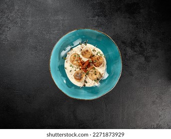 Fancy appetizer of grilled sea scallops in creamy sauce. Roasted sea scallops in cheese espuma in ceramic bowl on black concrete background. Seafood menu. Delicatessen sea scallop on dark stone table