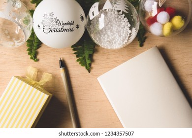 Fancy balls for decorate Christmas tree in New year eve festival and fern leaves on wooden table, which have blank notebook, pen and little gift box - Powered by Shutterstock