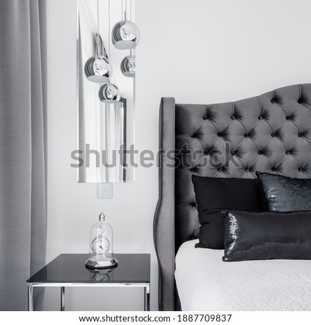 Fancy bedside table with decorative clock next to glamorous bed with quilted headboard