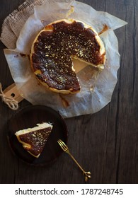 Fancy Burnt Basque Cheesecake Flatlay With Gold Flakes. Burnt Cheese Cake On Wooden Table. Cheesecake Quarantine Baking Trend.