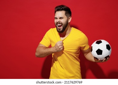 Fancy Charismatic Young Bearded Man Football Fan Pull Tear Yellow T-shirt Cheer Up Support Favorite Team Hold Soccer Ball Look Aside Scream Hooray Isolated On Plain Dark Red Background Studio Portrait