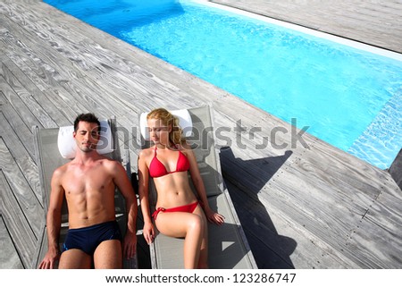 Fancy couple relaxing in longchairs by swimming pool