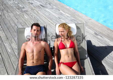 Fancy couple relaxing in longchairs by swimming pool