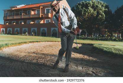 A fancy dapper mature black guy in an elegant outfit with trousers with suspenders, hat, tie, with a cigar in his mouth, is hitting the ball from a sand bunker zone of a golf field using an iron club