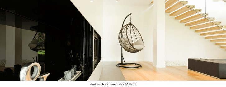 Fancy egg shaped chair swing in a trendy spacious lounge near the black shining commode with decorations