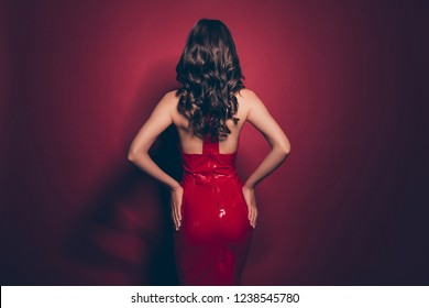 Fancy gorgeous attractive elegant graceful pretty brunette lady with modern hairstyle she stand back to the camera hold hands on hips her lustrous shine mini wear isolated on deep red background