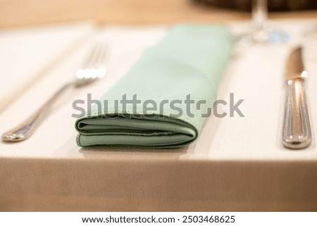 Fancy grreen textured and folded table cloth on dinner table with fork and knife close up